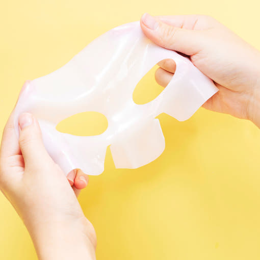 Hands holding a sheet mask against a yellow background