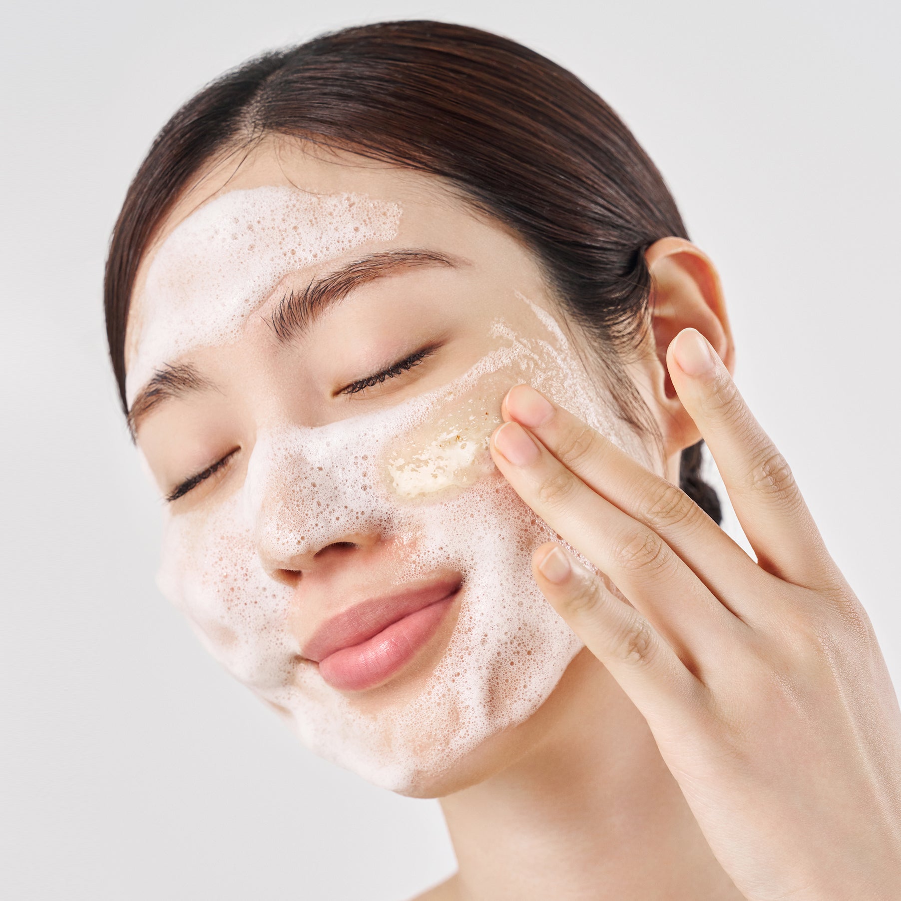 Woman applying Purito SEOUL Oat In Gentle Exfoliating Face Cleanser to her face with a neutral background