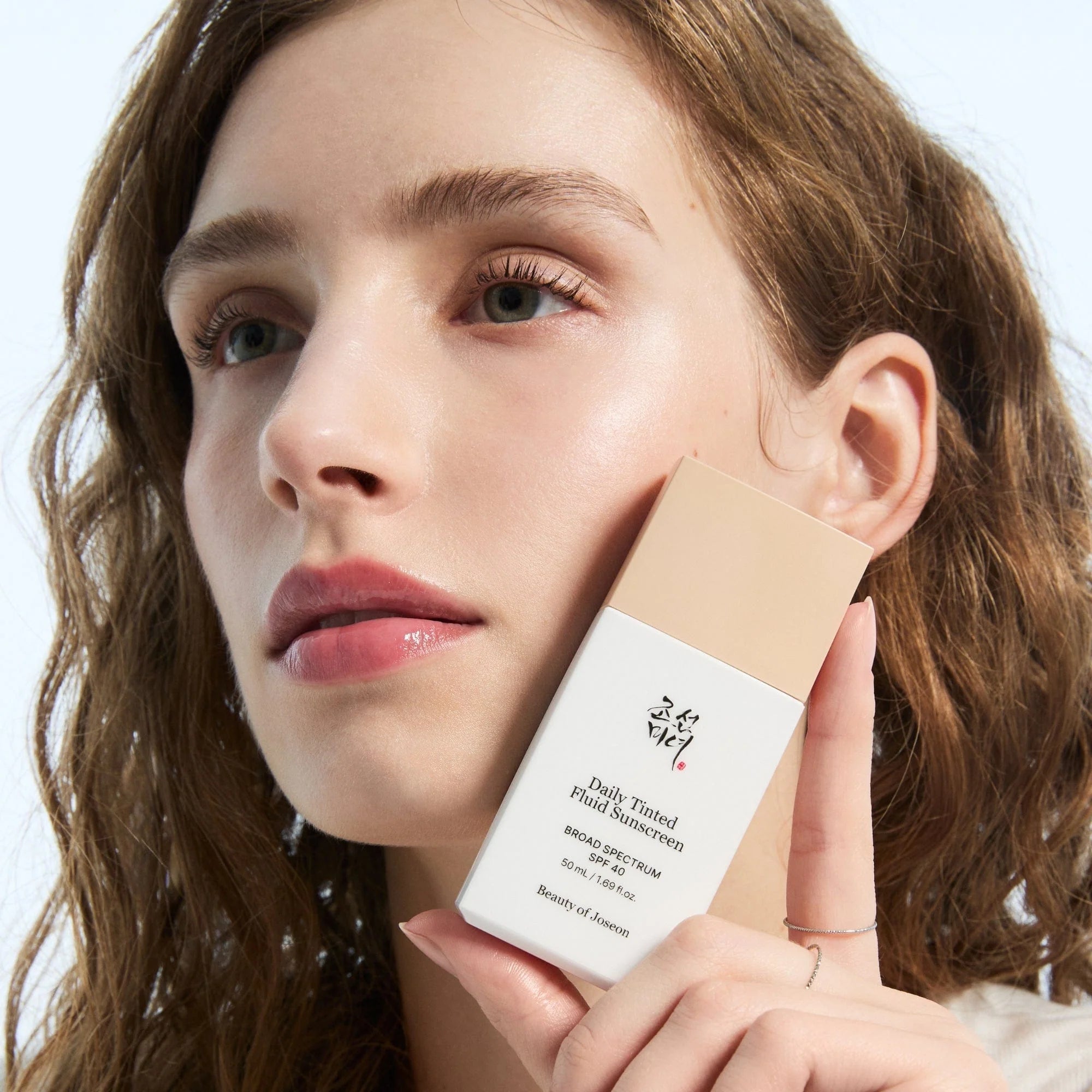 Woman holding a white container with text, against a neutral background