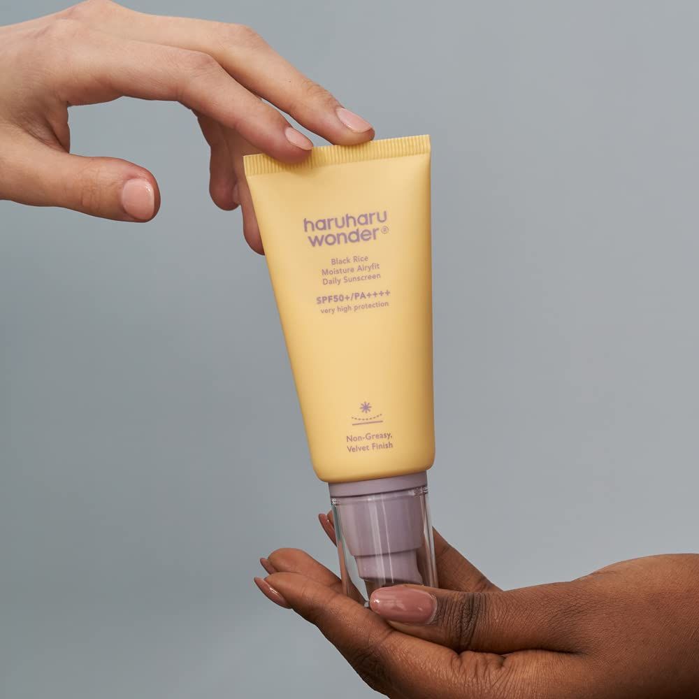 Hand holding a tube of Haruhu Wonder sunscreen against a gray background