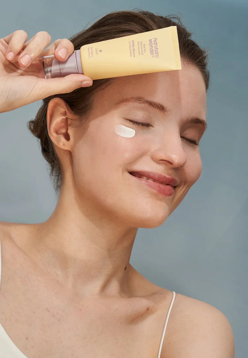 Woman applying sunscreen cream to her face with a gray background