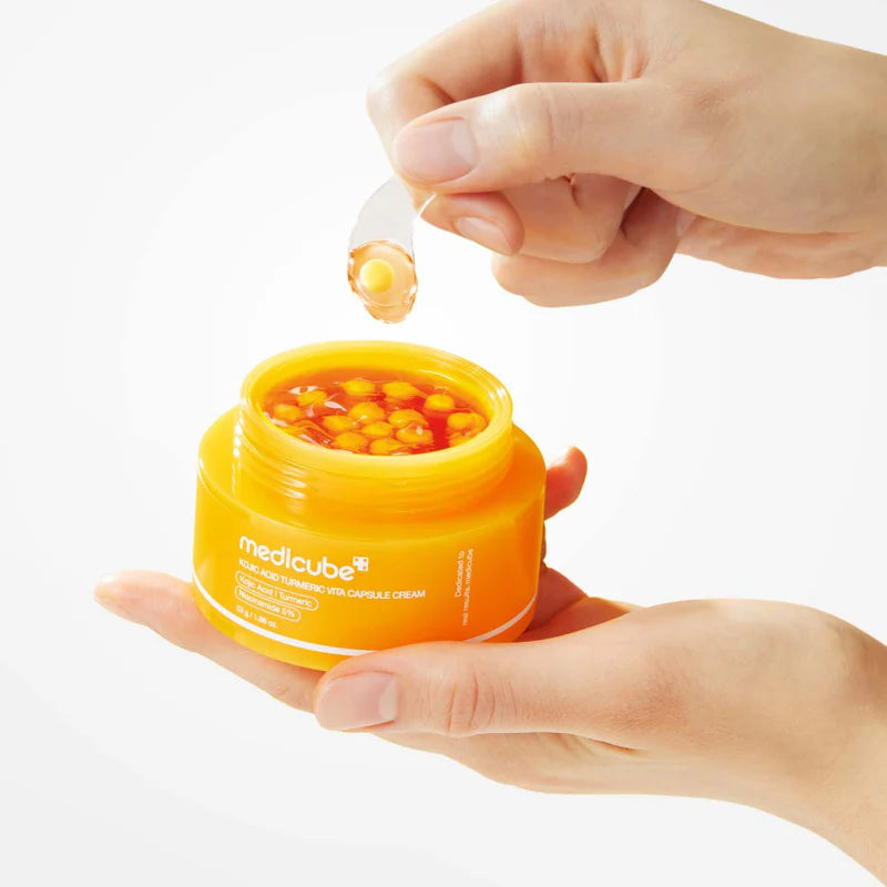 Orange jar of Medicube cream with a hand applying a drop to the skin.