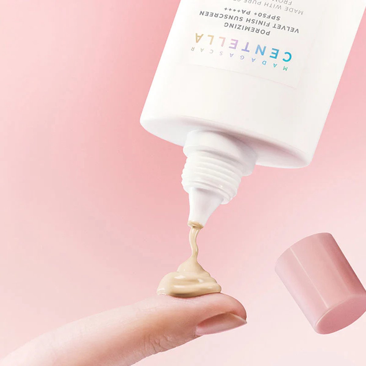 Tube of Centella Asiatica product with cream being squeezed onto a finger against a pink background